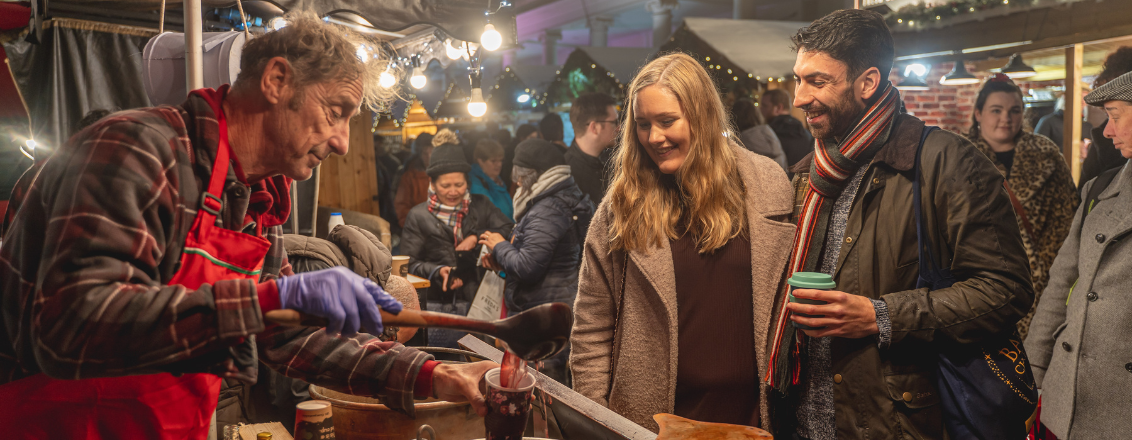 A man serving mulled wine to two people