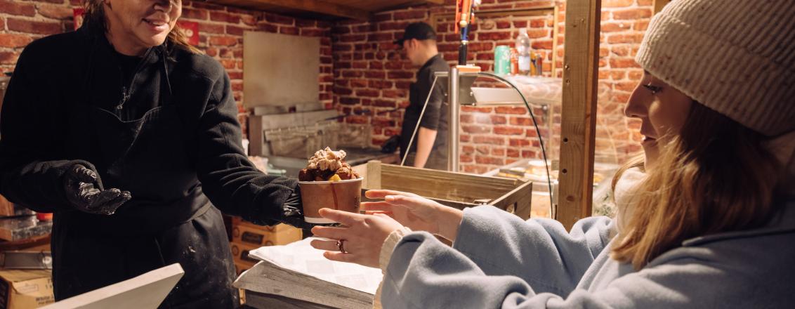 A trader handing over a tub of pigs in blankets to a customer